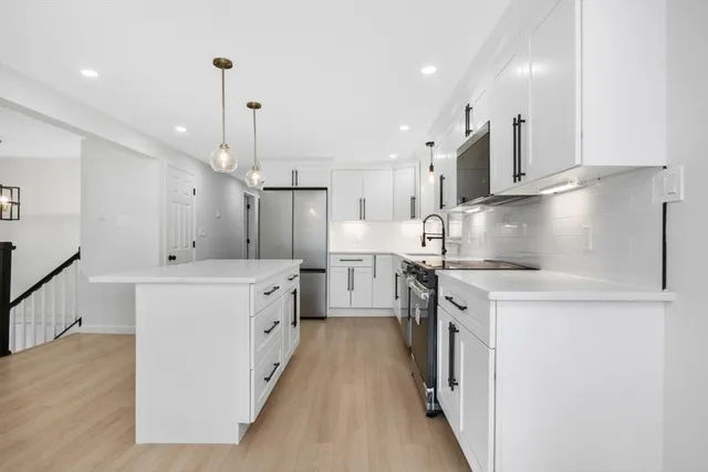 a kitchen with stainless steel appliances a stove a sink a refrigerator and white cabinets with wooden floor