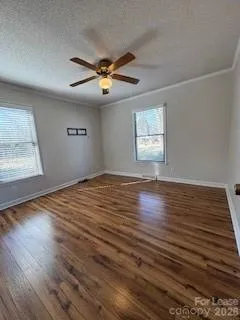 an empty room with wooden floor windows and fan