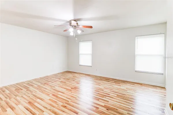 an empty room with wooden floor fan and windows