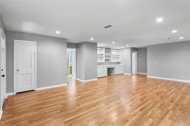 a view of an empty room with wooden floor and kitchen
