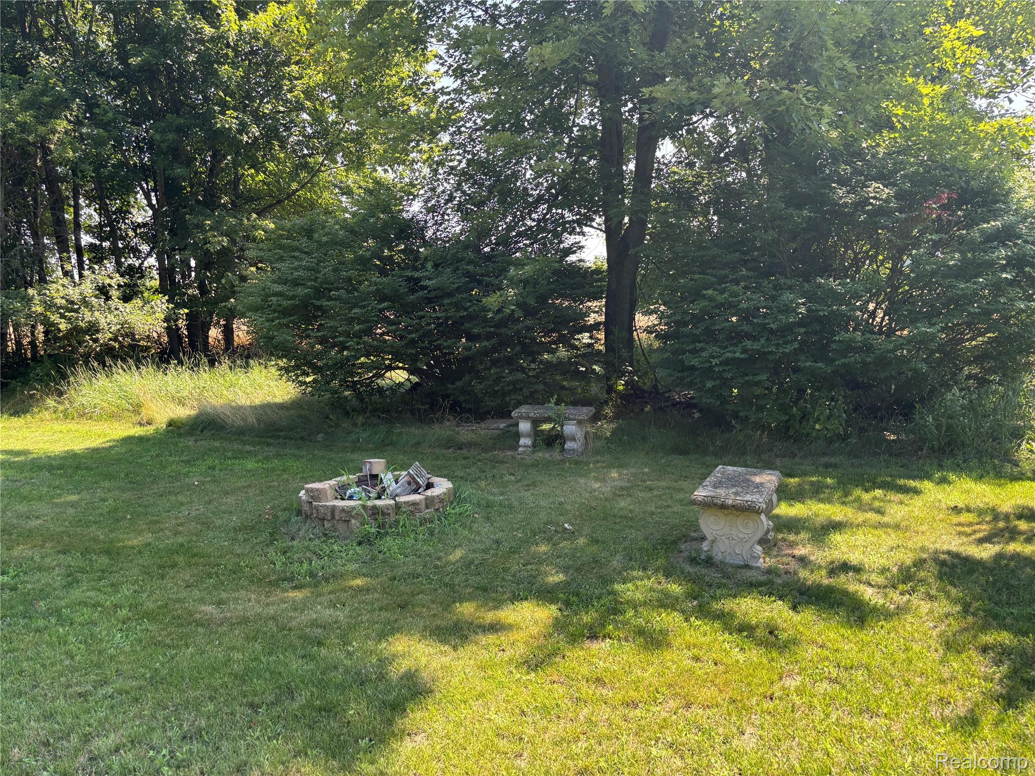 8531 South Waldron Road Pittsford, MI 49271 - Photo 36 of 40 Grassed yard with a stone fire pit and two stone benches, framed by mature trees and shrubs