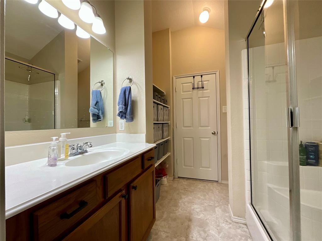 14044 Fontana Road Roanoke, TX 76262 - Photo 9 of 14 Single vanity with integrated sink and chrome faucet, wood-finish cabinetry, built-in shelving, and a glass-enclosed shower