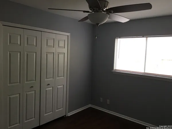 an empty room with wooden floor fan and windows