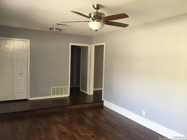 an empty room with wooden floor fan and windows