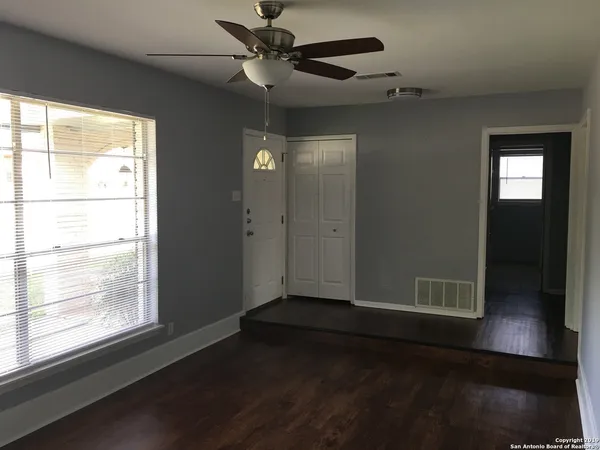 an empty room with wooden floor fan and windows