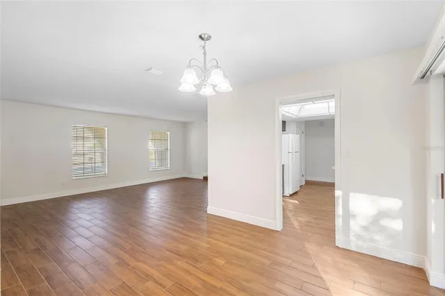 an empty room with wooden floor chandelier and windows