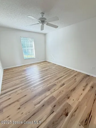 an empty room with wooden floor chandelier fan and windows