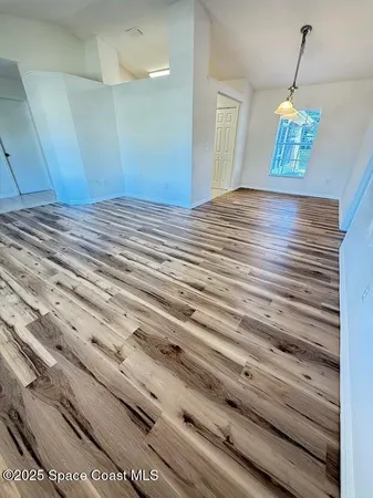 a view of empty room with wooden floor and kitchen view