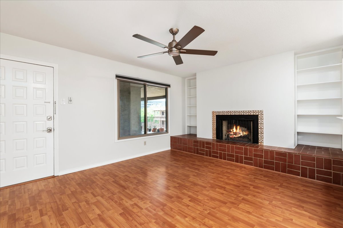 505 West 7th Street, Unit 313 Austin, TX 78701 - Photo 3 of 30 Unfurnished living room featuring a tiled fireplace, baseboards, built in shelves, wood finished floors, and ceiling fan
