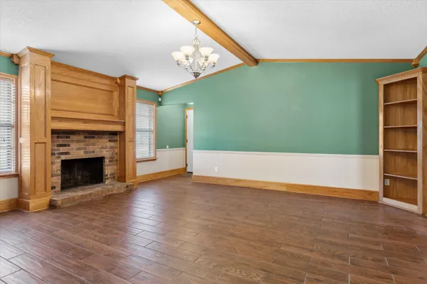 an empty room with wooden floor fireplace and windows