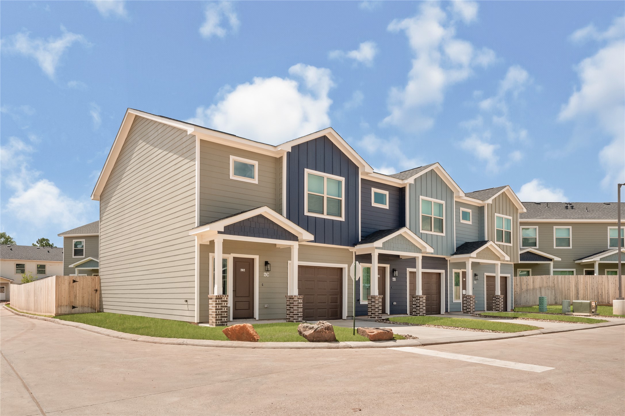 14010 Longstreet Road, Unit 2 Willis, TX 77318 - Photo 2 of 29 Modern townhouse with a two-story design, featuring a mix of beige and dark blue siding. It includes a small front yard, attached garage, and a paved driveway. The neighborhood has a clean, suburban feel with a fenced backyard.