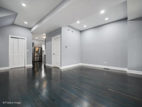 a view of an empty room with wooden floor and a kitchen