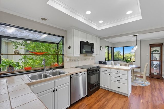 a kitchen with stainless steel appliances white cabinets large window and wooden floor