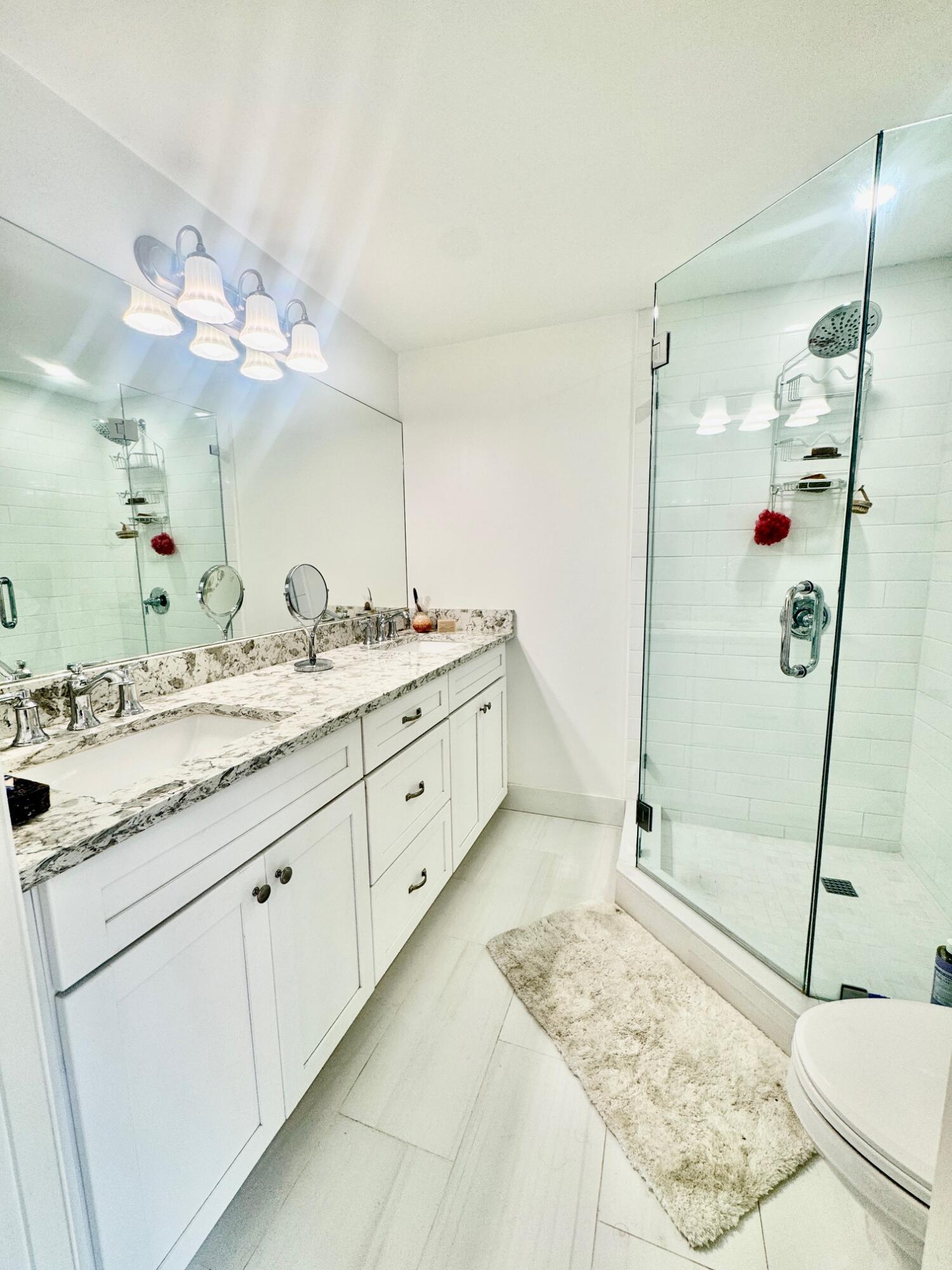 3105 31st Court, Unit 130D Jupiter, FL 33477 - Photo 12 of 24 a bathroom with a granite countertop sink a mirror and shower