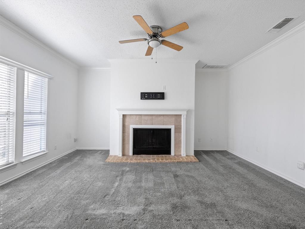 5310 Keller Springs Road, Unit 332 Dallas, TX 75248 - Photo 13 of 39 Unfurnished living room with carpet floors, a tiled fireplace, a ceiling fan, a textured ceiling, and ornamental molding