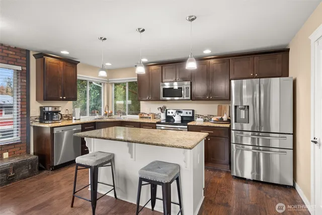 a kitchen with stainless steel appliances granite countertop a refrigerator a stove top oven a sink dishwasher and white cabinets with wooden floor