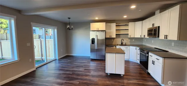 a kitchen with stainless steel appliances granite countertop a refrigerator a sink dishwasher a stove and a microwave oven on the wooden floor