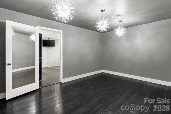 an empty room with wooden floor chandelier and windows