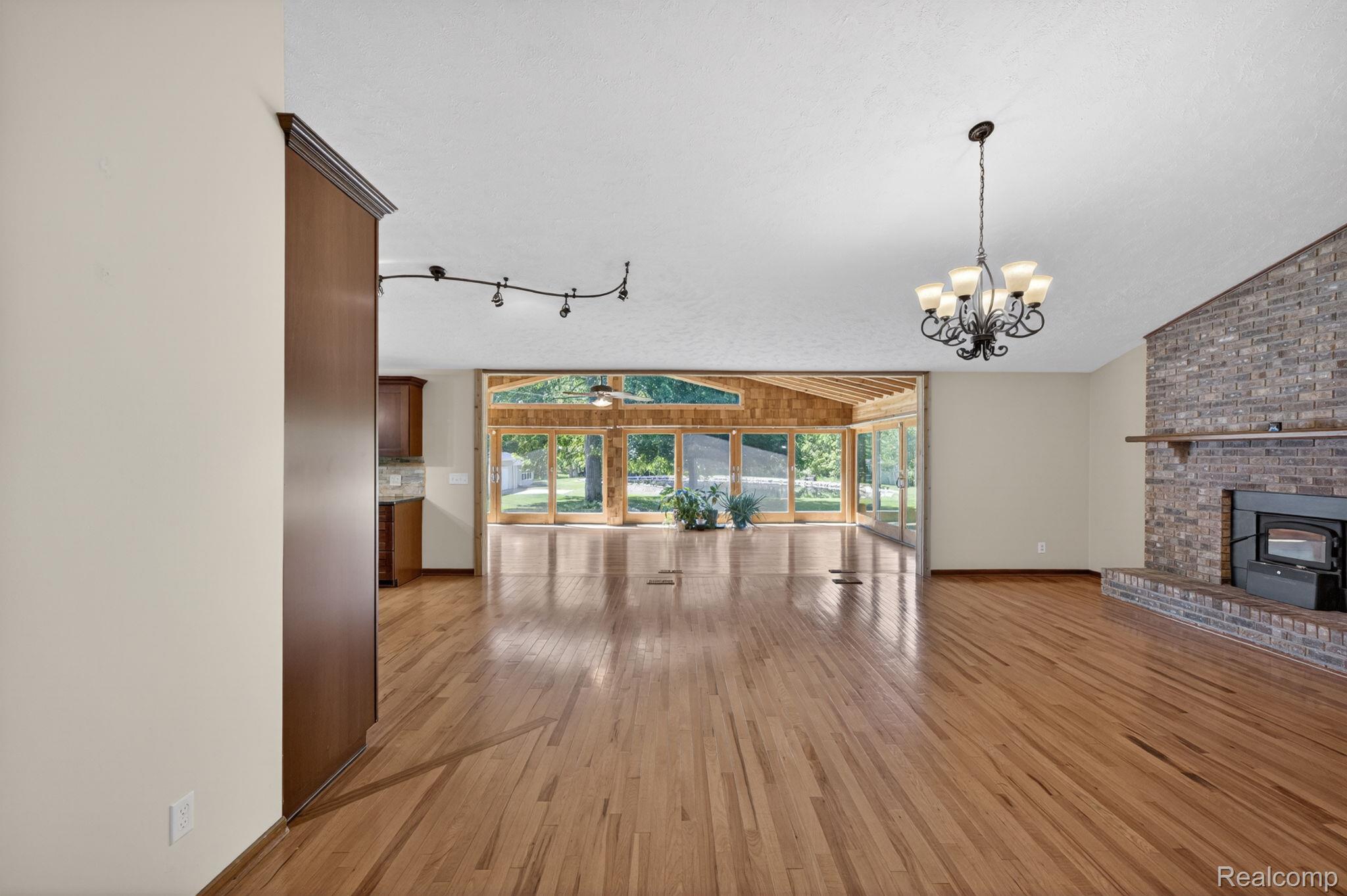 9353 Hill Road Swartz Creek, MI 48473 - Photo 31 of 98 Spacious interior featuring wood-finish flooring, a brick fireplace with a wood-burning insert, and a prominent chandelier