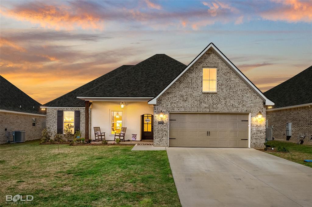 Traditional home with brick siding, driveway, a front lawn, covered porch, and roof with shingles