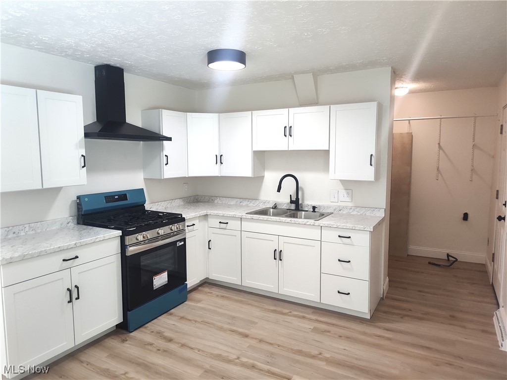 8016 Ninevah Road Geneva, OH 44041 - Photo 23 of 45 Kitchen featuring stainless steel gas range, white cabinets, a textured ceiling, wall chimney range hood, and light countertops