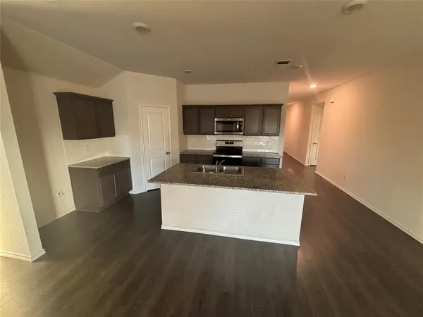a living room with stainless steel appliances a fireplace a flat screen tv and a sink