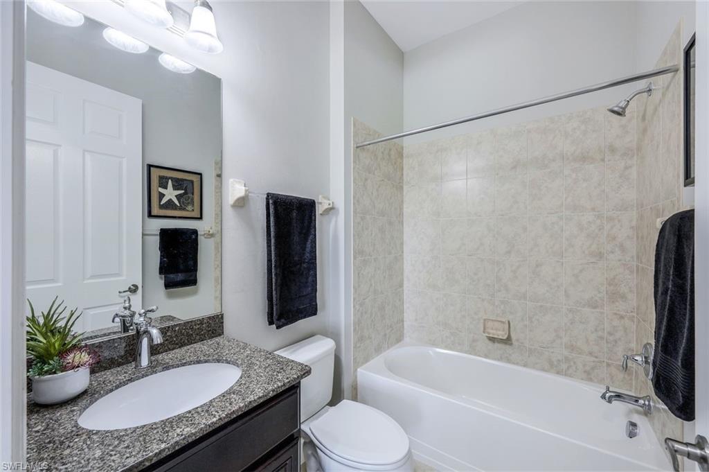 9062 Limestone Lane Naples, FL 34120 - Photo 18 of 48 a bathroom with a granite countertop sink toilet a mirror a shower and a bathtub