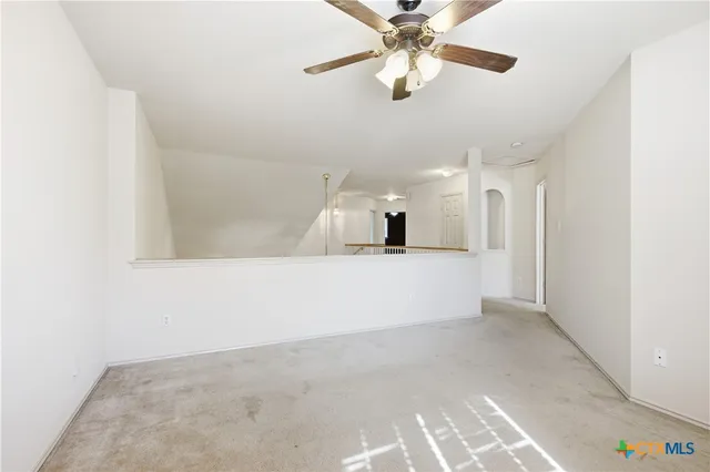 an empty room with a chandelier fan and wooden floor