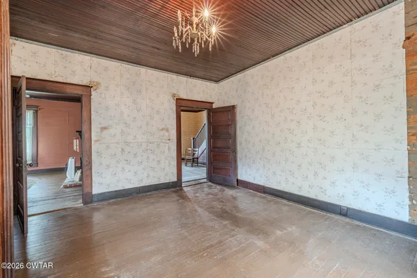 an empty room with wooden floor chandelier fan and windows