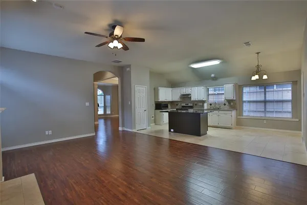 a view of an empty room and kitchen with wooden floor and a ceiling fan