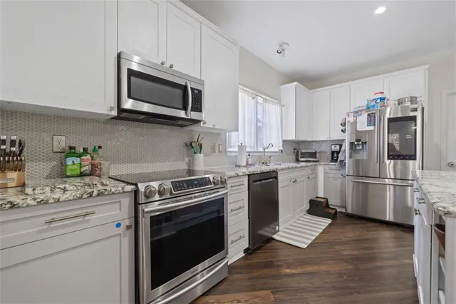 a kitchen with stainless steel appliances white cabinets a stove a microwave a refrigerator a sink and dishwasher with wooden floor