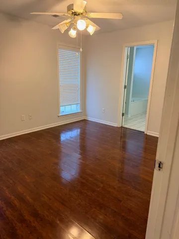a view of an empty room with wooden floor and fan