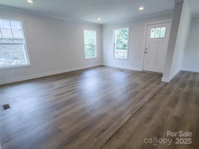 a view of an empty room with wooden floor and a window