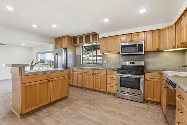 a kitchen with stainless steel appliances kitchen island granite countertop a sink and dishwasher a stove top oven with wooden floor