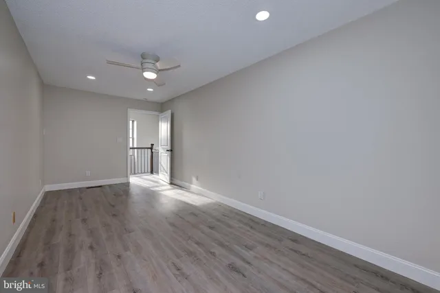 a view of an empty room with wooden floor and a ceiling fan