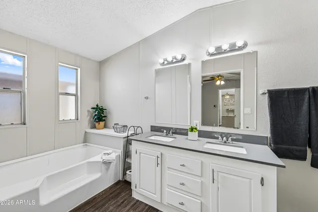 a bathroom with a granite countertop double vanity sink a mirror a bathtub and window