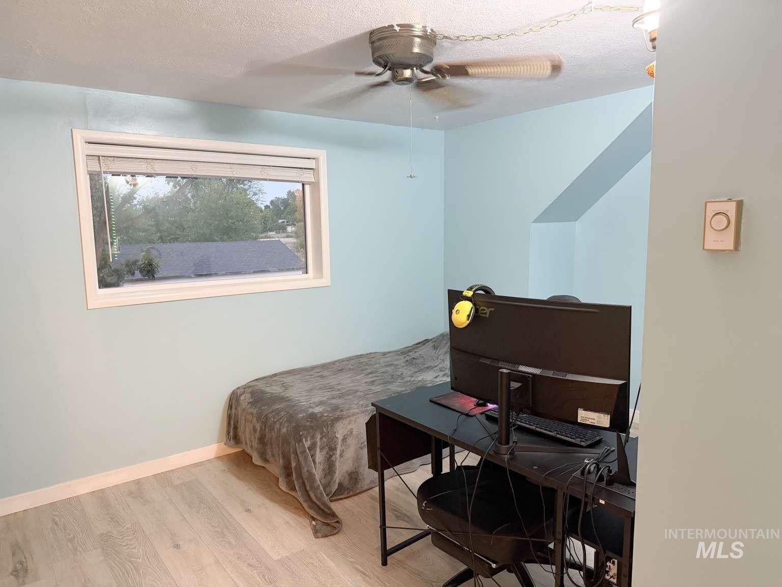 1158 South Powerline Road Nampa, ID 83686 - Photo 26 of 46 Room featuring light blue walls, wood-finish flooring, a white-framed window, and a ceiling fan with integrated lighting