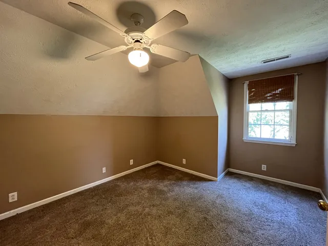 an empty room with a chandelier fan and windows