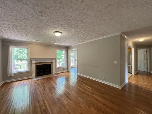 a view of an empty room with wooden floor fireplace and a window