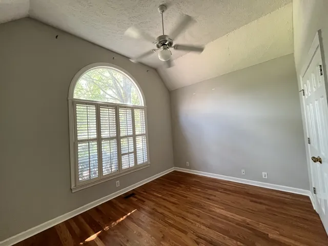 an empty room with wooden floor fan and windows