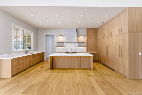 a large white kitchen with a large counter top a sink a window and stainless steel appliances