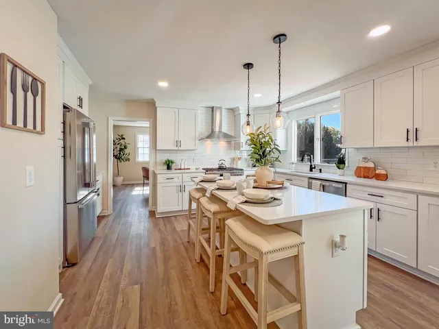a kitchen with stainless steel appliances kitchen island granite countertop a refrigerator a sink dishwasher a stove and white countertops with wooden floor