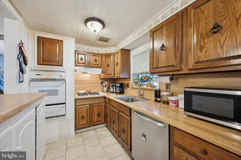 a kitchen with stainless steel appliances granite countertop a stove top oven a sink dishwasher and a refrigerator with wooden cabinets