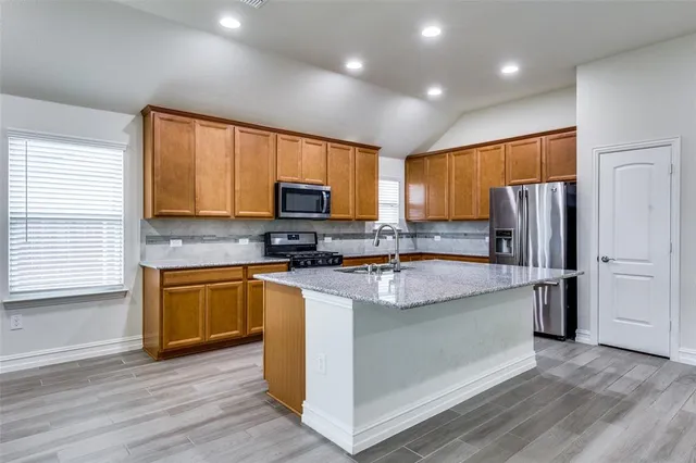 a kitchen with stainless steel appliances granite countertop a refrigerator a stove top oven a sink dishwasher and wooden floor