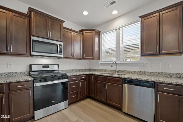 a kitchen with stainless steel appliances granite countertop wooden cabinets granite counter tops and a window