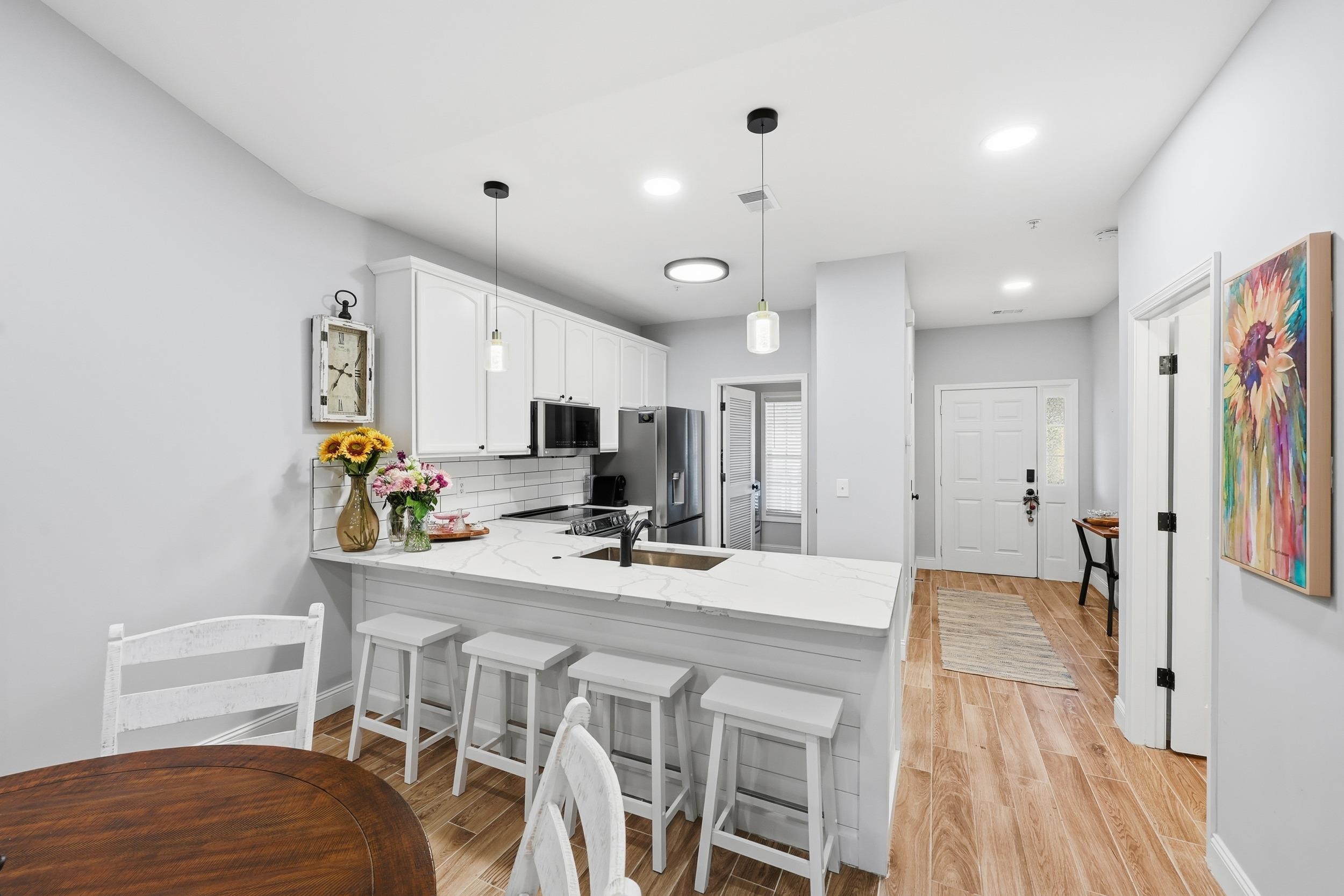 5810 Longwood Drive, Unit 303 Murrells Inlet, SC 29576 - Photo 3 of 27 Kitchen featuring a kitchen breakfast bar, white cabinetry, a peninsula, light stone counters, and pendant lighting
