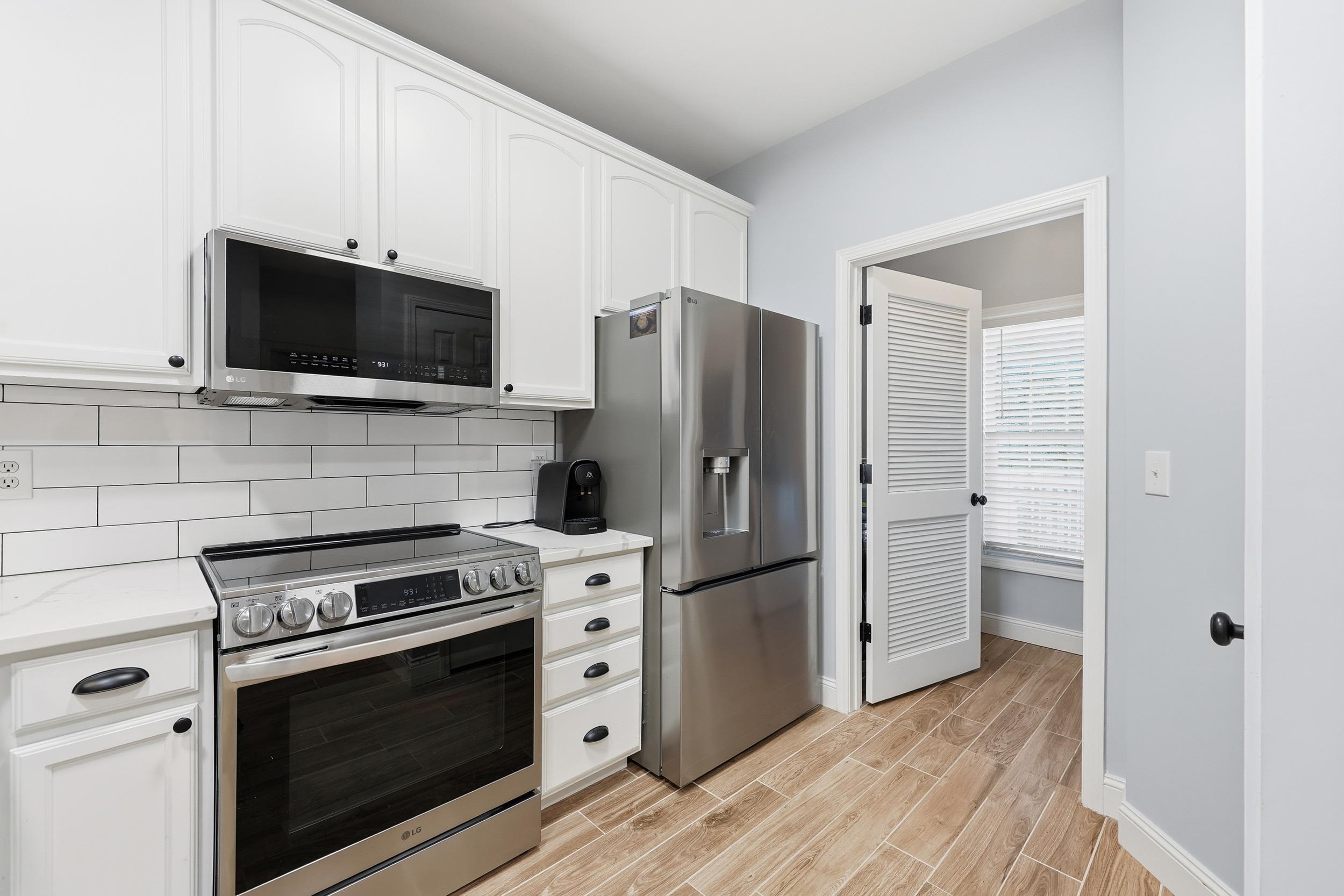 5810 Longwood Drive, Unit 303 Murrells Inlet, SC 29576 - Photo 7 of 27 Kitchen featuring stainless steel appliances, white cabinets, wood tiled floors, decorative backsplash, and light stone counters