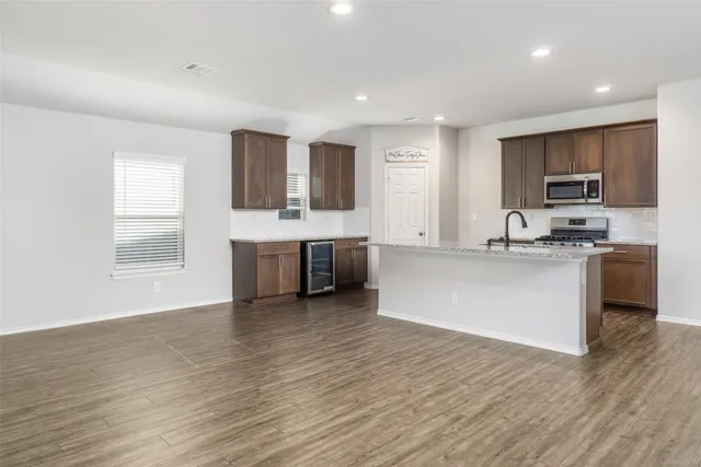 a large kitchen with stainless steel appliances granite countertop a stove top oven a sink dishwasher and white cabinets with wooden floor