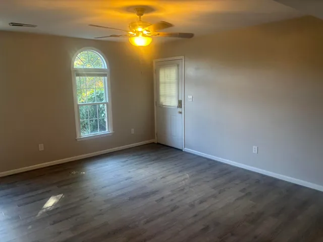 an empty room with wooden floor fan and windows