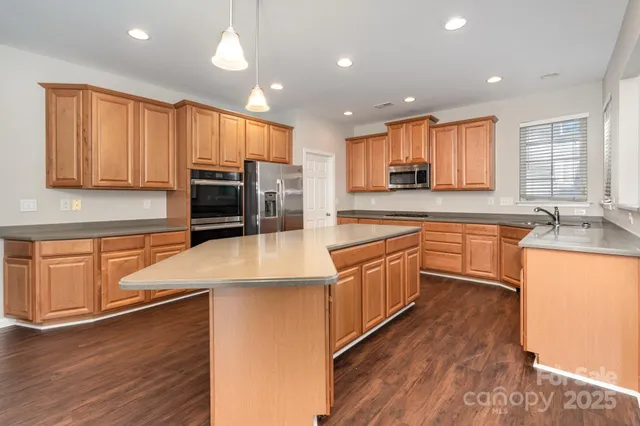 a large kitchen with stainless steel appliances granite countertop a stove a sink a refrigerator and white cabinets with wooden floor